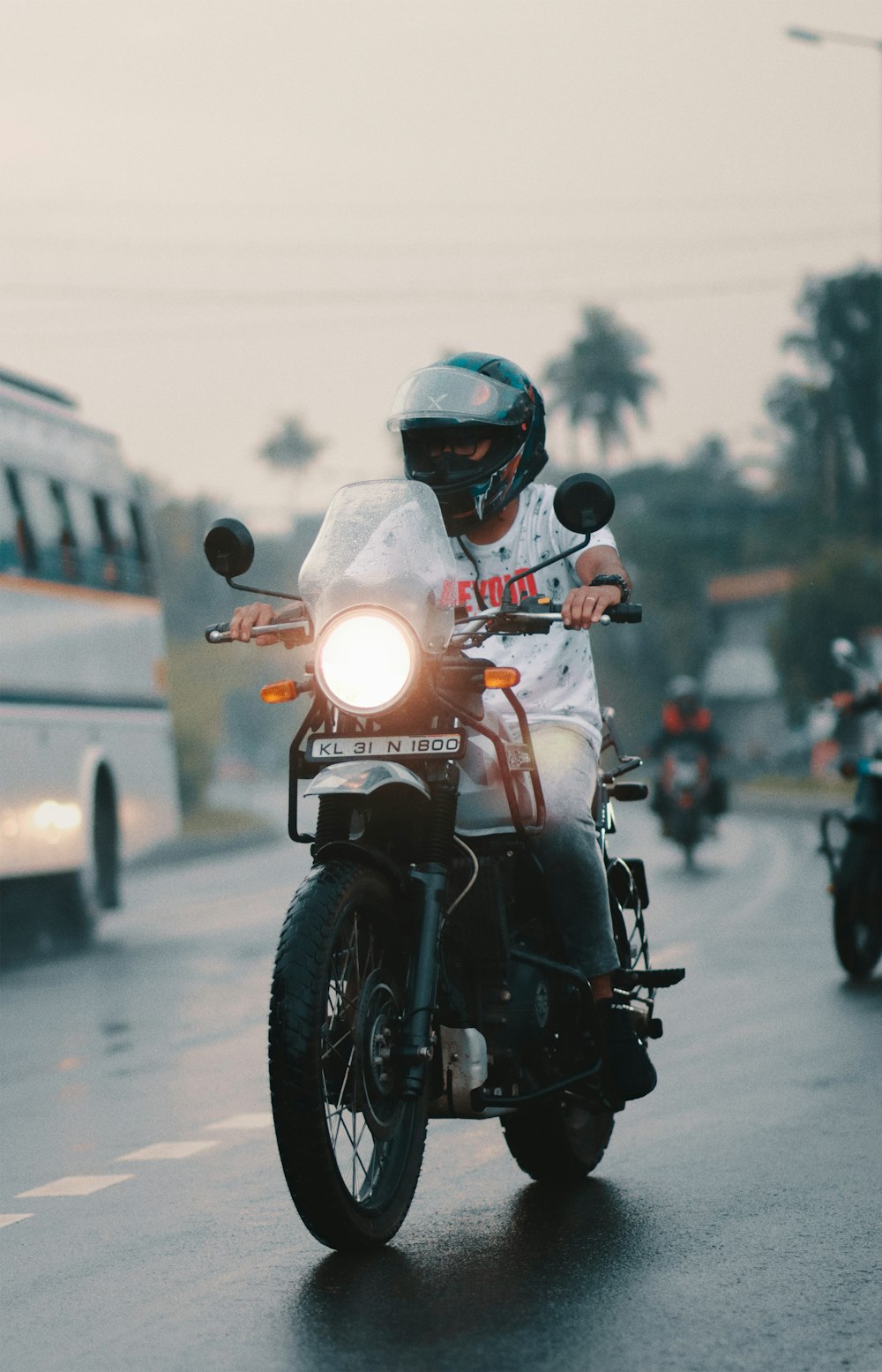 a man riding a motorcycle down a street next to a bus