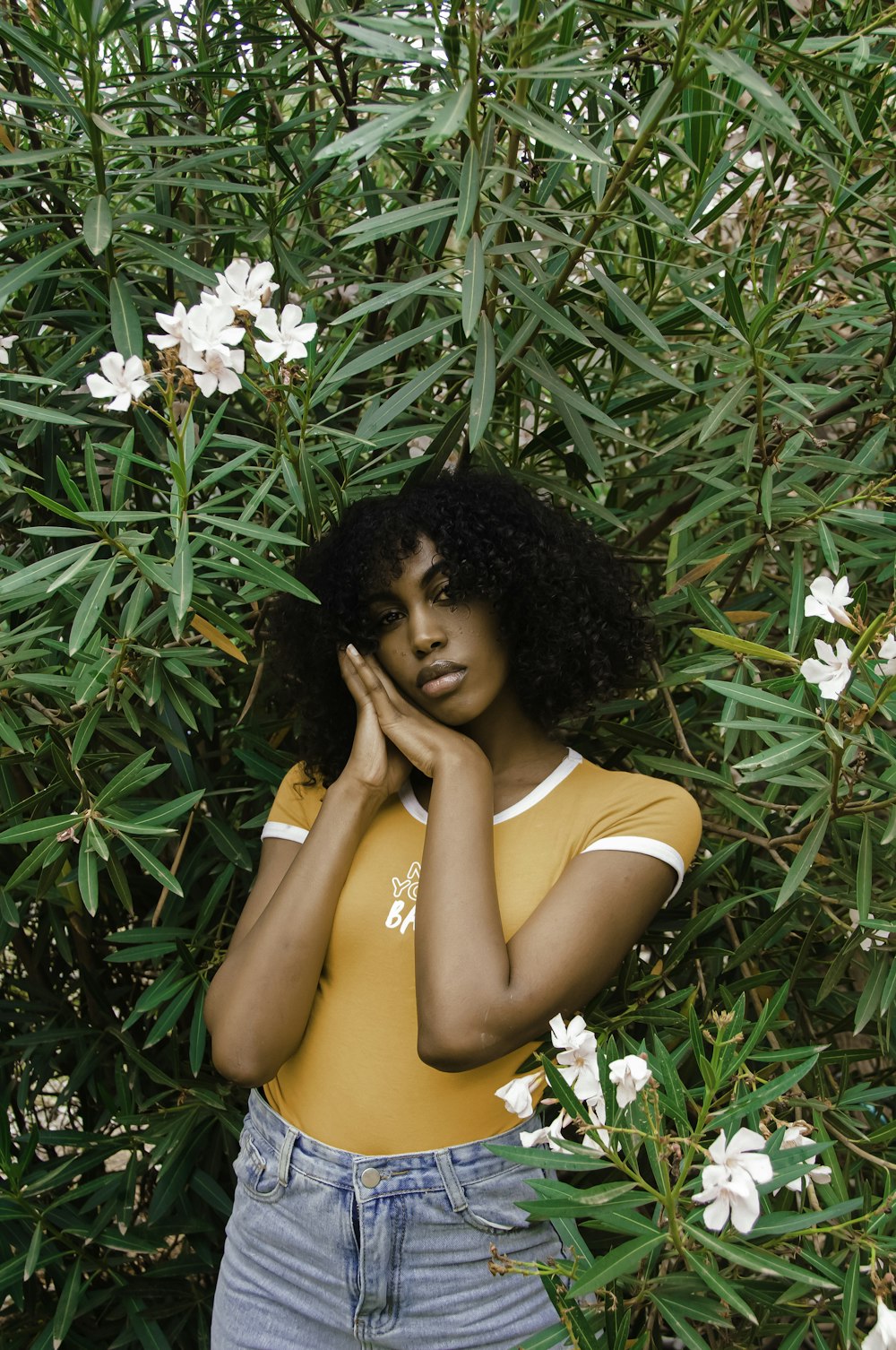 a woman standing in front of a bush with white flowers