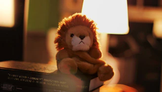 A soft crocheted lion with a fluffy mane sitting on a wooden shelf.