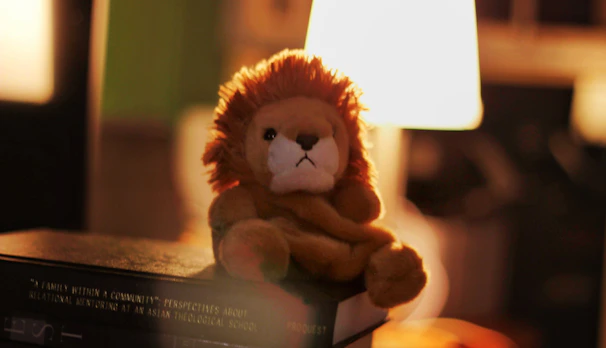 A soft crocheted lion with a fluffy mane sitting on a wooden shelf.