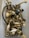 A collection of assorted metal hardware, including handles, knobs, and screws, placed loosely inside a plastic container. The objects are primarily made of brass with some white ceramic elements, and a few pieces are painted black or feature different metallic finishes.