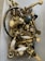A collection of assorted metal hardware, including handles, knobs, and screws, placed loosely inside a plastic container. The objects are primarily made of brass with some white ceramic elements, and a few pieces are painted black or feature different metallic finishes.