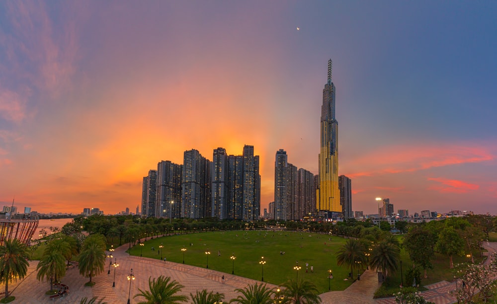 a city skyline with tall buildings and a green field