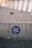 A circular blue sticker with the words 'Good Karma' and 'Rework' is affixed to a concrete surface. The background features a blurred, repetitive pattern suggesting steps or seating rows, likely in an outdoor setting. The ground in front of the concrete appears rough and slightly littered.