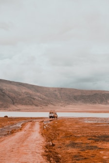 a truck driving down a dirt road next to a body of water