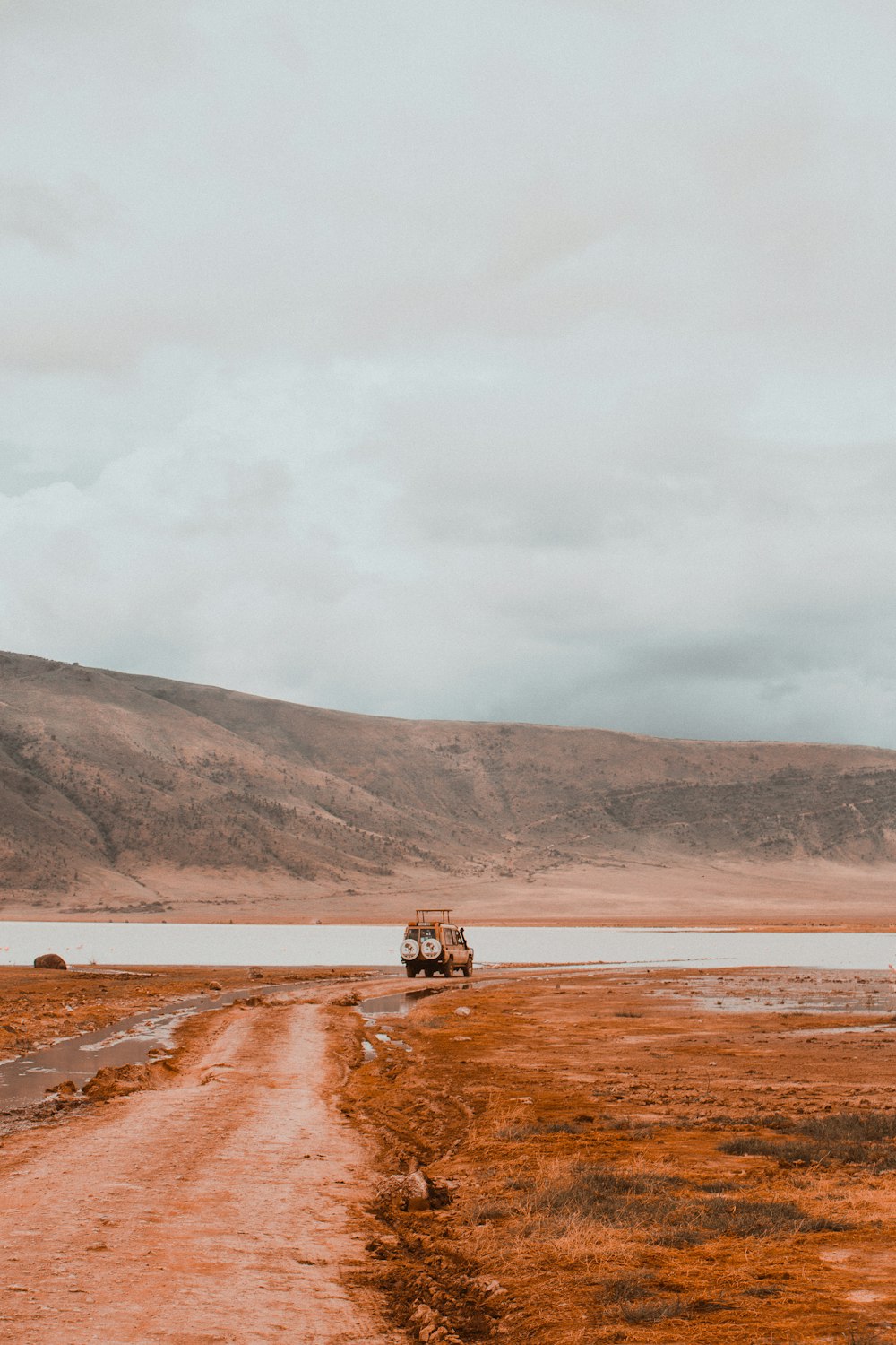a truck driving down a dirt road next to a body of water