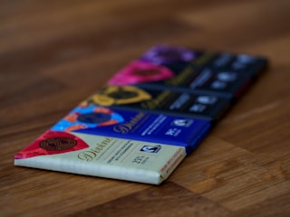 Close-up of a variety of colorful protein bars stacked on a rustic wooden table.