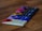 A collection of chocolate bars arranged in a row on a wooden surface. Each bar has distinctive, colorful packaging, with visible text and designs on the covers. The focus is on the closest bar, which features cream and red colors, while the others progressively blur into the background.