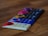 A collection of chocolate bars arranged in a row on a wooden surface. Each bar has distinctive, colorful packaging, with visible text and designs on the covers. The focus is on the closest bar, which features cream and red colors, while the others progressively blur into the background.