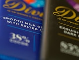 Two chocolate bar wrappers are positioned side by side, one visibly labeled as smooth milk chocolate with salted caramel and the other described as exquisite dark chocolate. Both wrappers feature elegant cursive typography.
