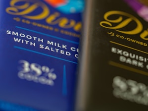 Two chocolate bar wrappers are positioned side by side, one visibly labeled as smooth milk chocolate with salted caramel and the other described as exquisite dark chocolate. Both wrappers feature elegant cursive typography.