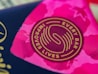 A close-up view of a circular logo with the words 'Every Bar Improves Lives' written around a stylized design. The background displays vibrant shades of pink with abstract patterns, possibly floral or star-like shapes.