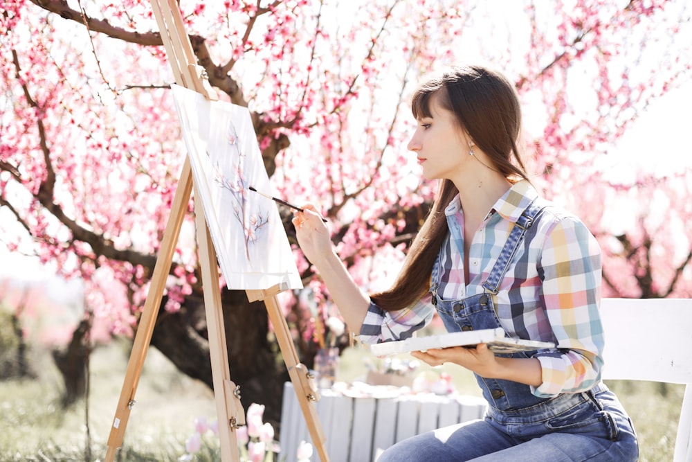 Una mujer sentada frente a un cerezo pintando un cuadro