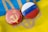 Two circular badges are displayed, one with the Soviet hammer and sickle on a red background, and the other featuring the Russian flag with horizontal stripes of white, blue, and red. They are placed on top of a textile with the colors and pattern resembling the Ukrainian flag.