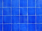 A pattern of blue tiles arranged in a grid. Each tile is square and the grout lines are visible between them, creating a geometric and orderly design.