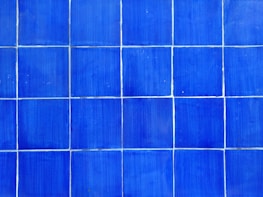 A pattern of blue tiles arranged in a grid. Each tile is square and the grout lines are visible between them, creating a geometric and orderly design.