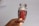 A hand holding a clear glass jar filled with red saffron threads against a plain background. The jar has a decorative gold rim on its lid.