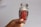 A hand holding a clear glass jar filled with red saffron threads against a plain background. The jar has a decorative gold rim on its lid.