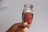 A hand holding a clear glass jar filled with red saffron threads against a plain background. The jar has a decorative gold rim on its lid.