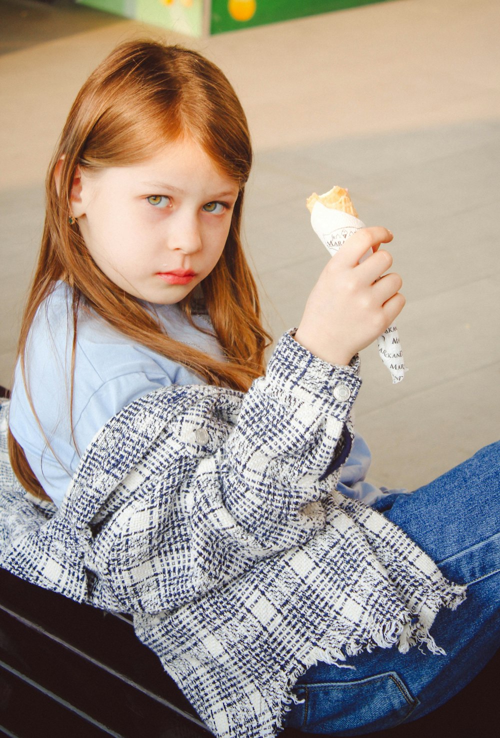 a little girl sitting on a bench eating something