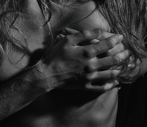 A black and white photograph focusing on hands and hair placed over a bare chest. The lighting emphasizes the texture of the skin and the strands of hair, creating dramatic shadows and highlights.