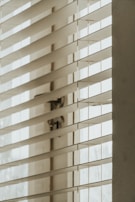 Close-up of sleek white blinds partially open, casting gentle shadows on a wooden floor.