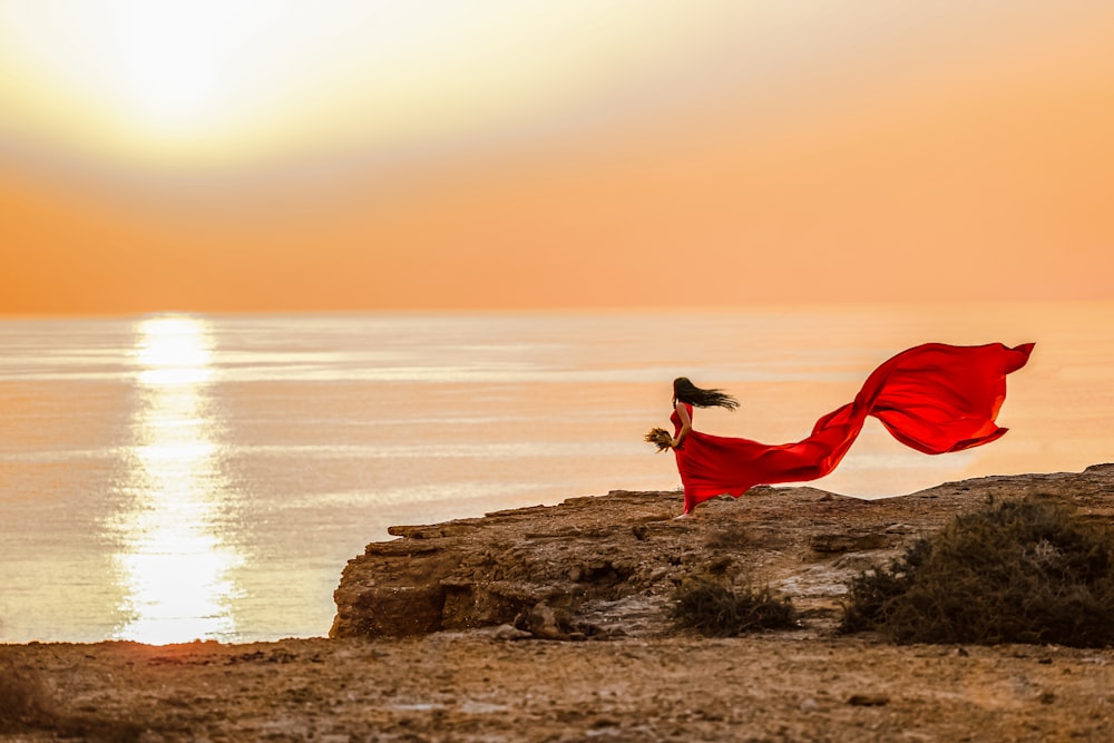 a woman in a red dress is standing on a rock