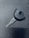 A single car key rests on a textured dark surface. The key has a black plastic head with a distinct shape and a metal blade exhibiting grooves specific to its locking mechanism.