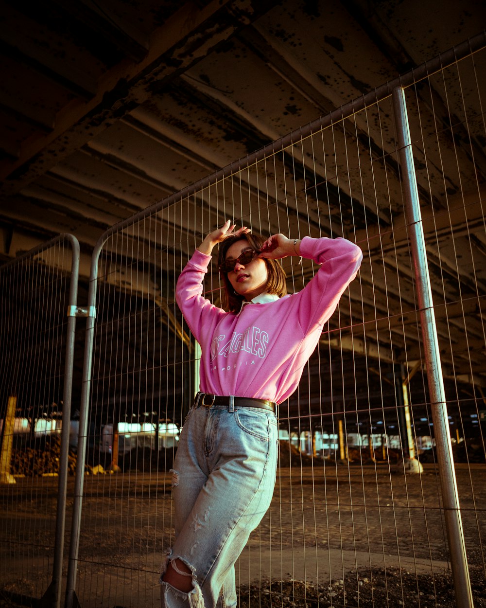 a woman in a pink shirt leaning against a fence