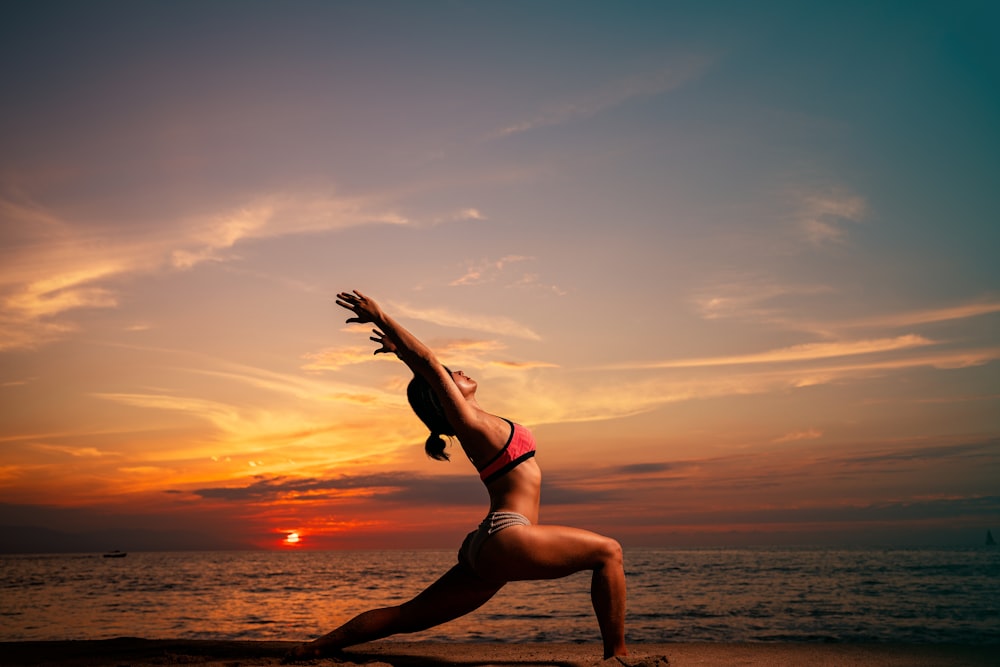 a woman in a bikini doing a yoga pose on the beach
