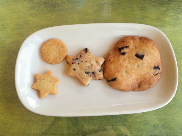 A colorful assortment of four cookie varieties arranged on a white plate with a cozy kitchen background