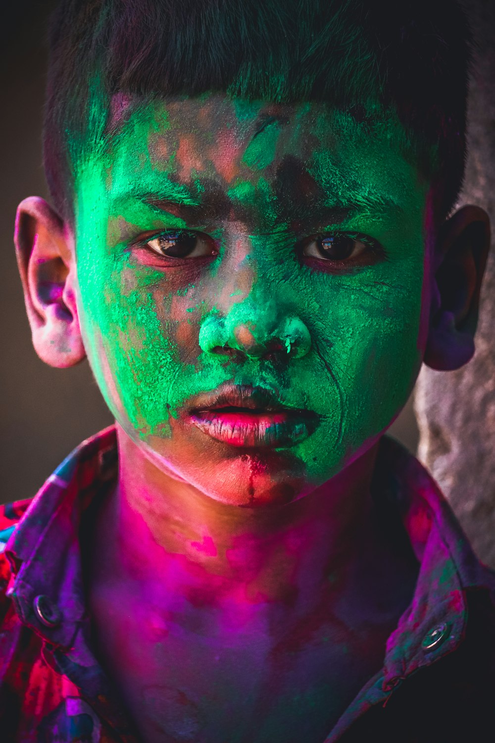 a young boy with green and pink paint on his face