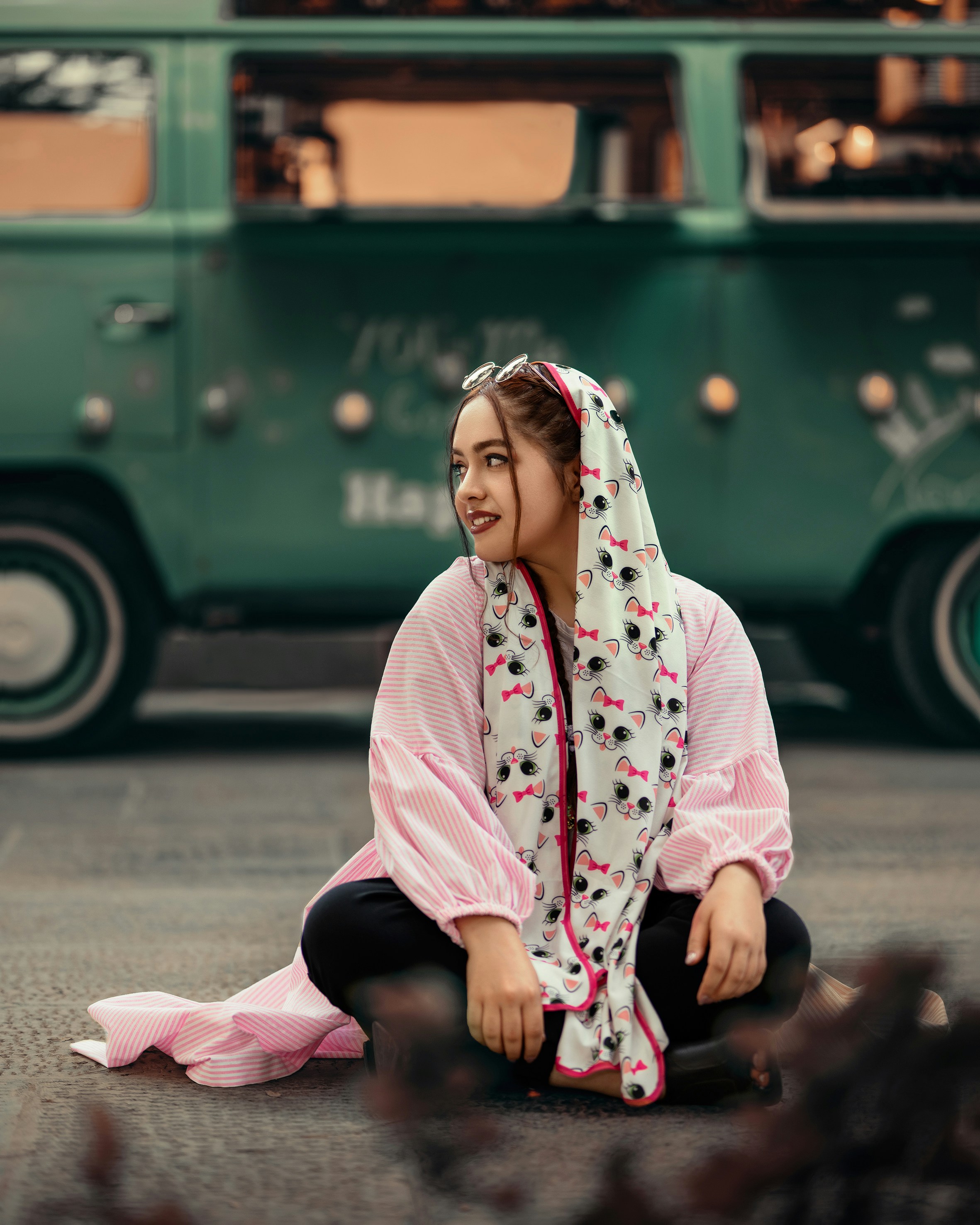 a woman sitting on the ground in front of a green bus