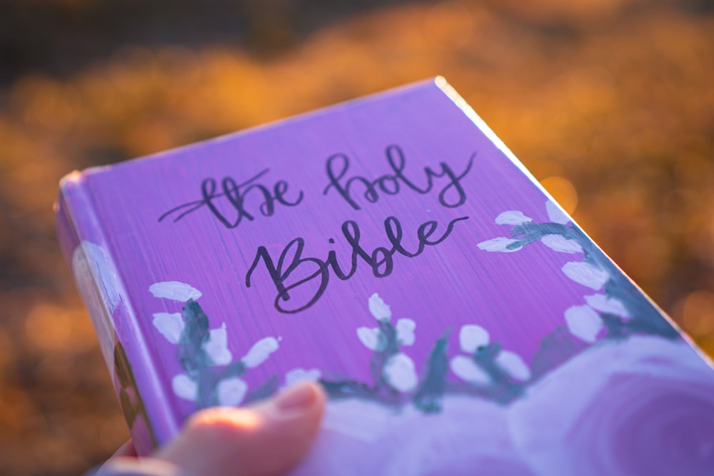 a person holding a purple book with the words the holy bible written on it