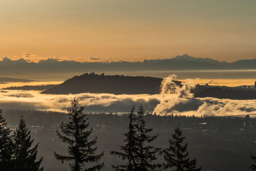 the sun is setting over the mountains and fog