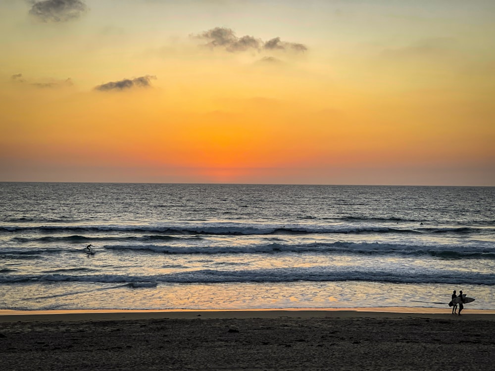 a couple of people standing on top of a beach next to the ocean