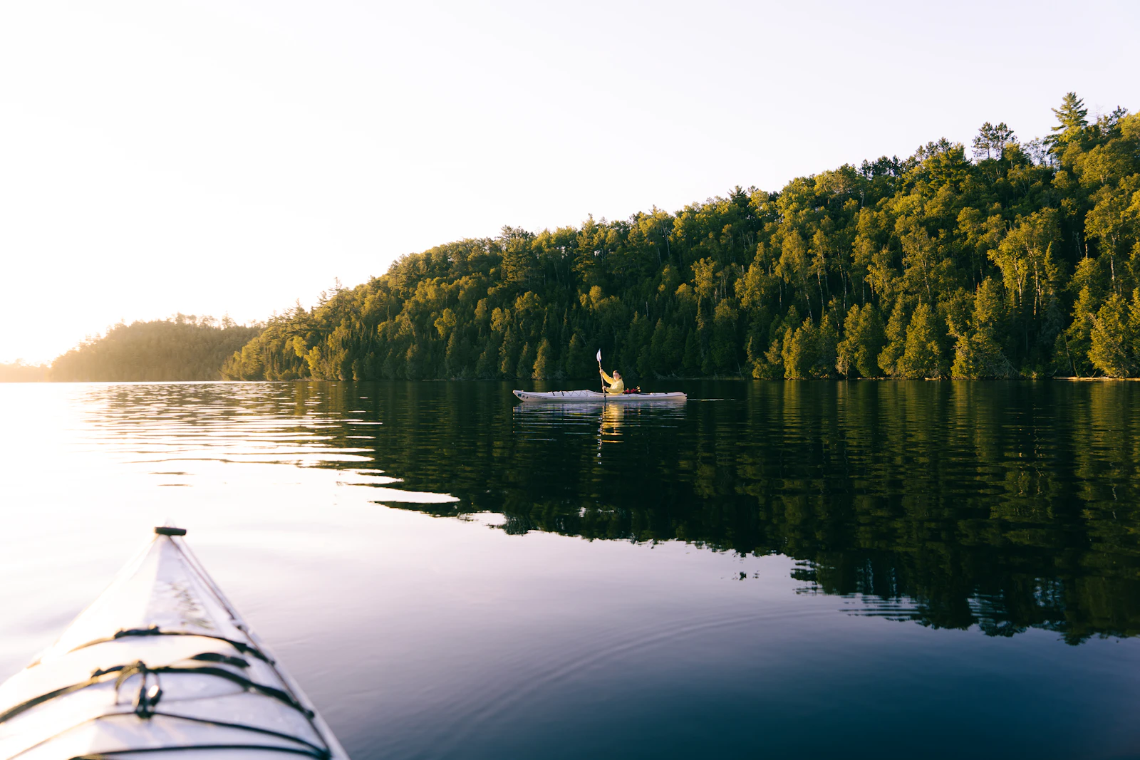 Person paddling a kayak across a calm lake at sunrise toward the horizon