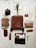 A neatly arranged collection of vintage and rustic items laid out on a textured, crumpled fabric backdrop. The centerpiece is a large brown leather backpack surrounded by a Polaroid camera, a leather-bound notebook, a wooden box filled with photographs, a small leather pouch, and scissors. A dried floral arrangement rests on an open book, adding a natural element to the composition.
