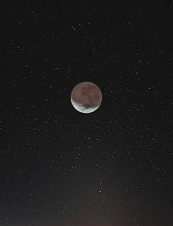 A crescent moon is visible in the center of a star-filled night sky. The sky is dotted with numerous small, twinkling stars, creating a serene and expansive celestial scene.