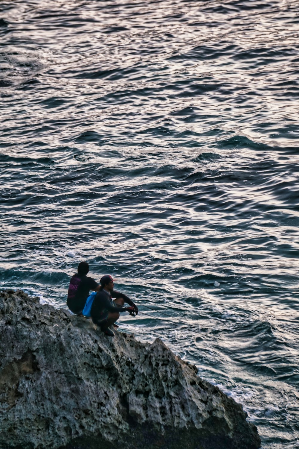 a couple of people sitting on top of a rock next to the ocean