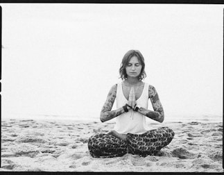 a woman sitting in a yoga position on the beach