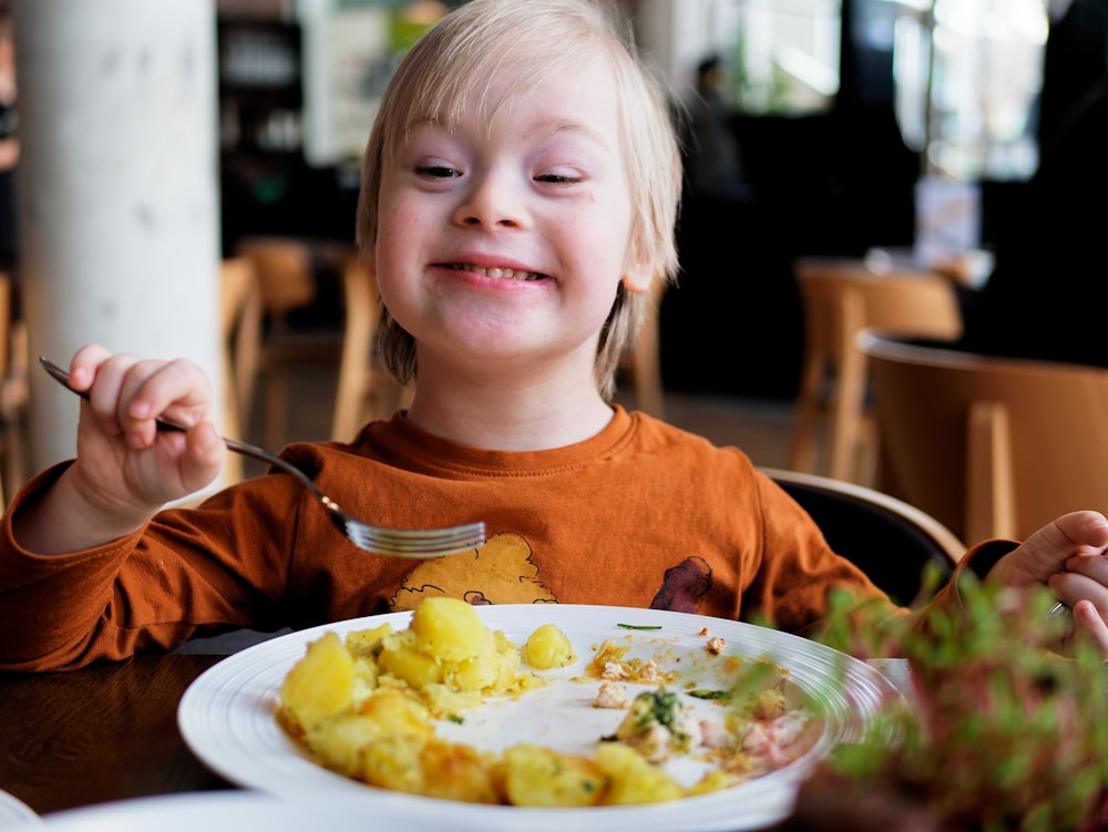 Ein kleiner Junge sitzt an einem Tisch mit einem Teller Essen