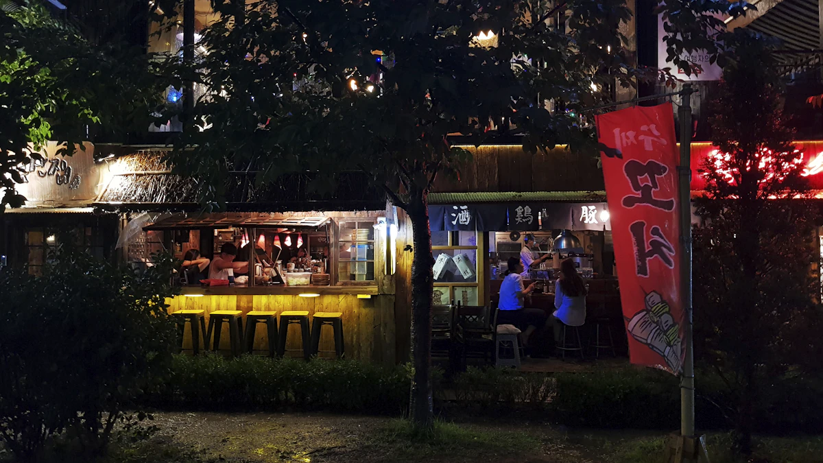 Small bar fronts with lit windows and red banners behind street trees on a Hongdae street at night