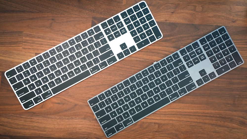 two computer keyboards sitting on top of a wooden table