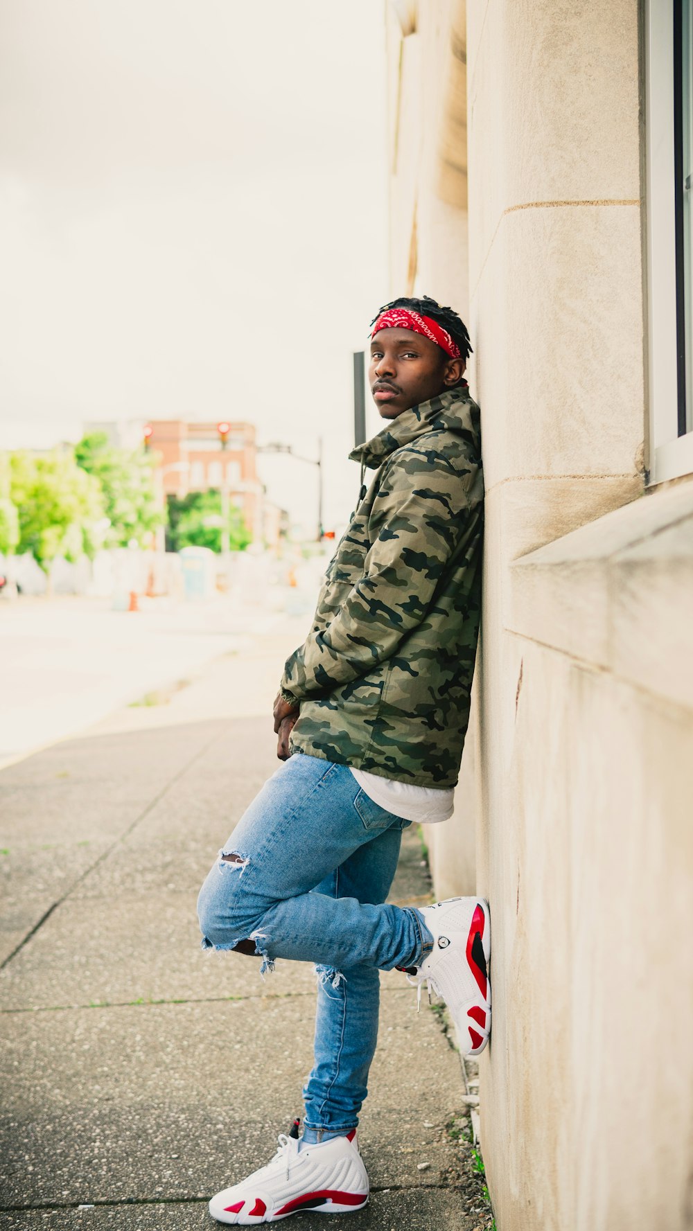 a man leaning against a wall wearing a green camo jacket