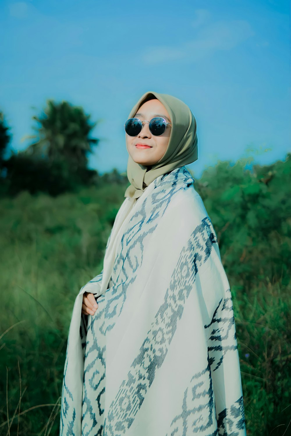 a woman wearing a hijab and sunglasses standing in a field