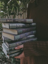 A smiling reader holding a pile of pre-loved books outside in natural light.