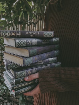 A smiling reader holding a pile of pre-loved books outside in natural light.