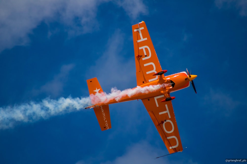 a small orange airplane flying through a blue sky