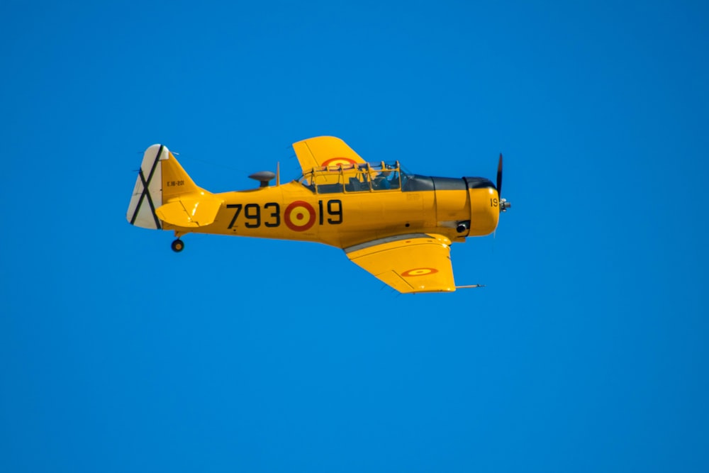 a small yellow airplane flying through a blue sky